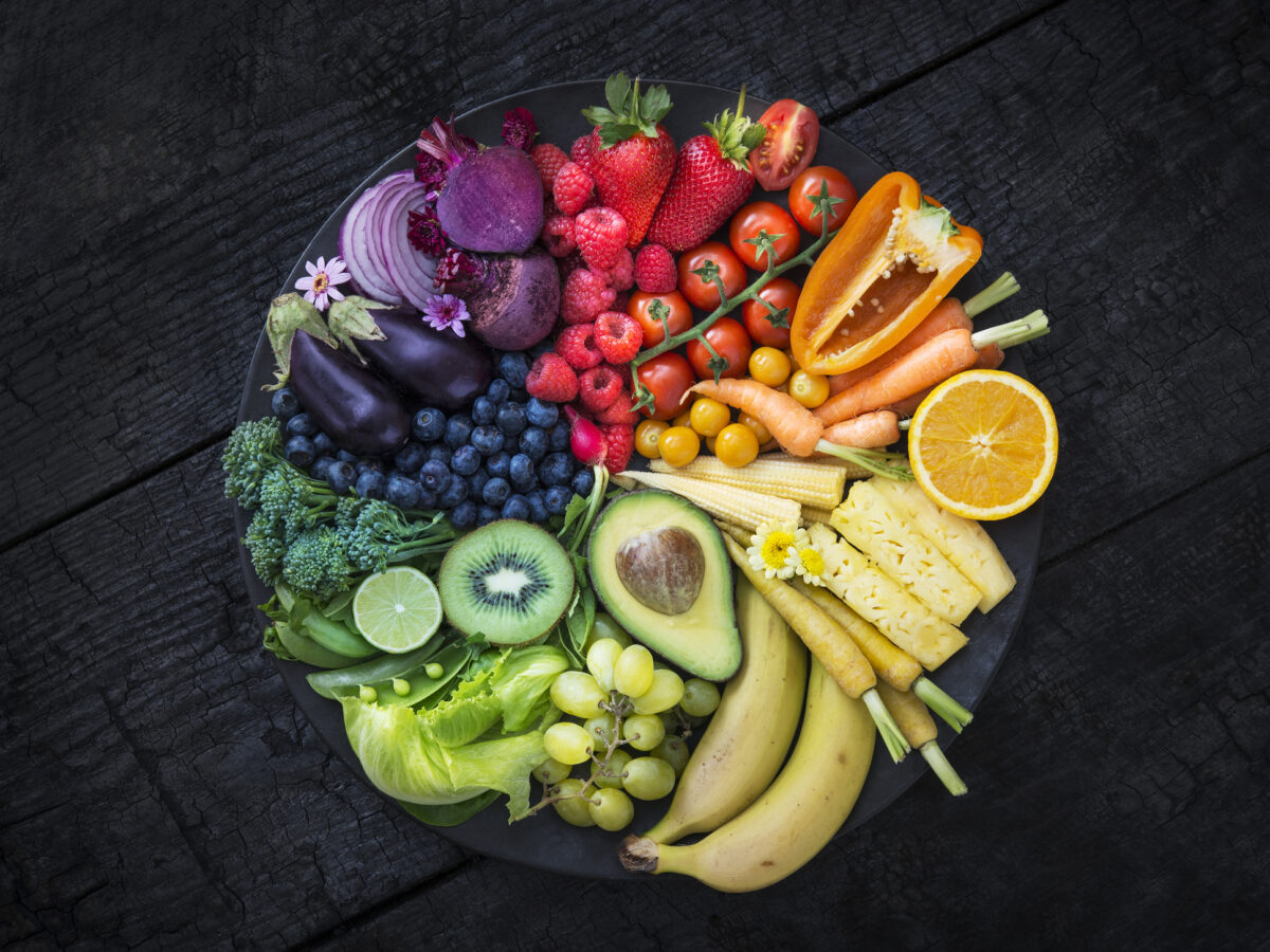 Multicoloured fruit and vegetables in a black bowl on a burnt surface.