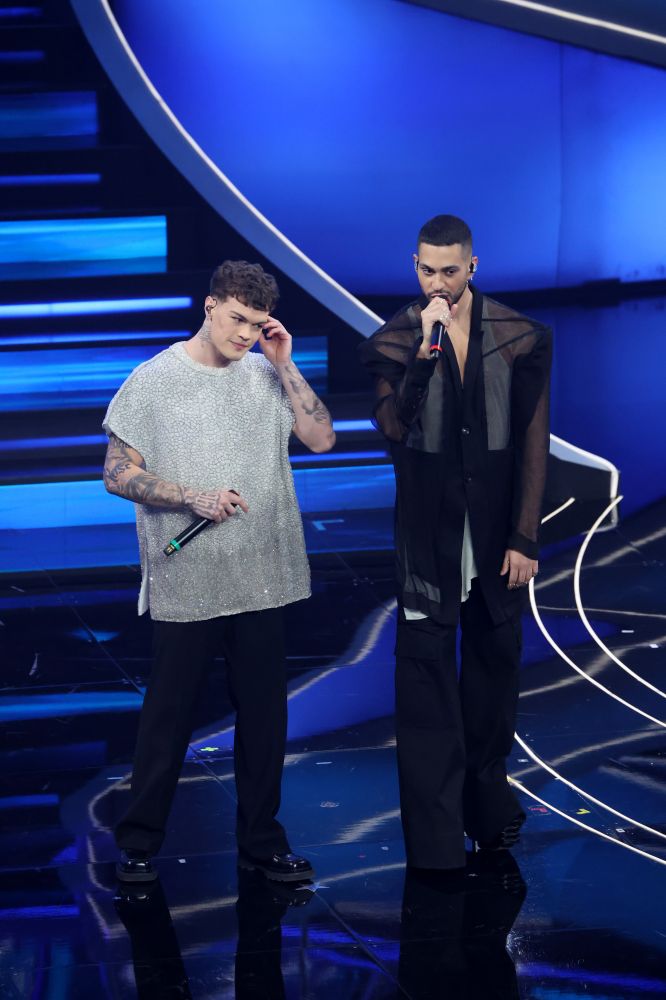 Mahmood e Blanco vincitori del Festival di Sanremo 2022 riportano sul palco dell’Ariston la canzone vincitrice “Brividi”. Mahmood indossa un completo total black di Rick Owens con una silhouette scultorea e trasparente e gli iconici stivali platform Kiss. Blanco invece per il duetto si presenta con un look Dolce & Gabbana con top bianco scintillante tappezzato di swarovski.