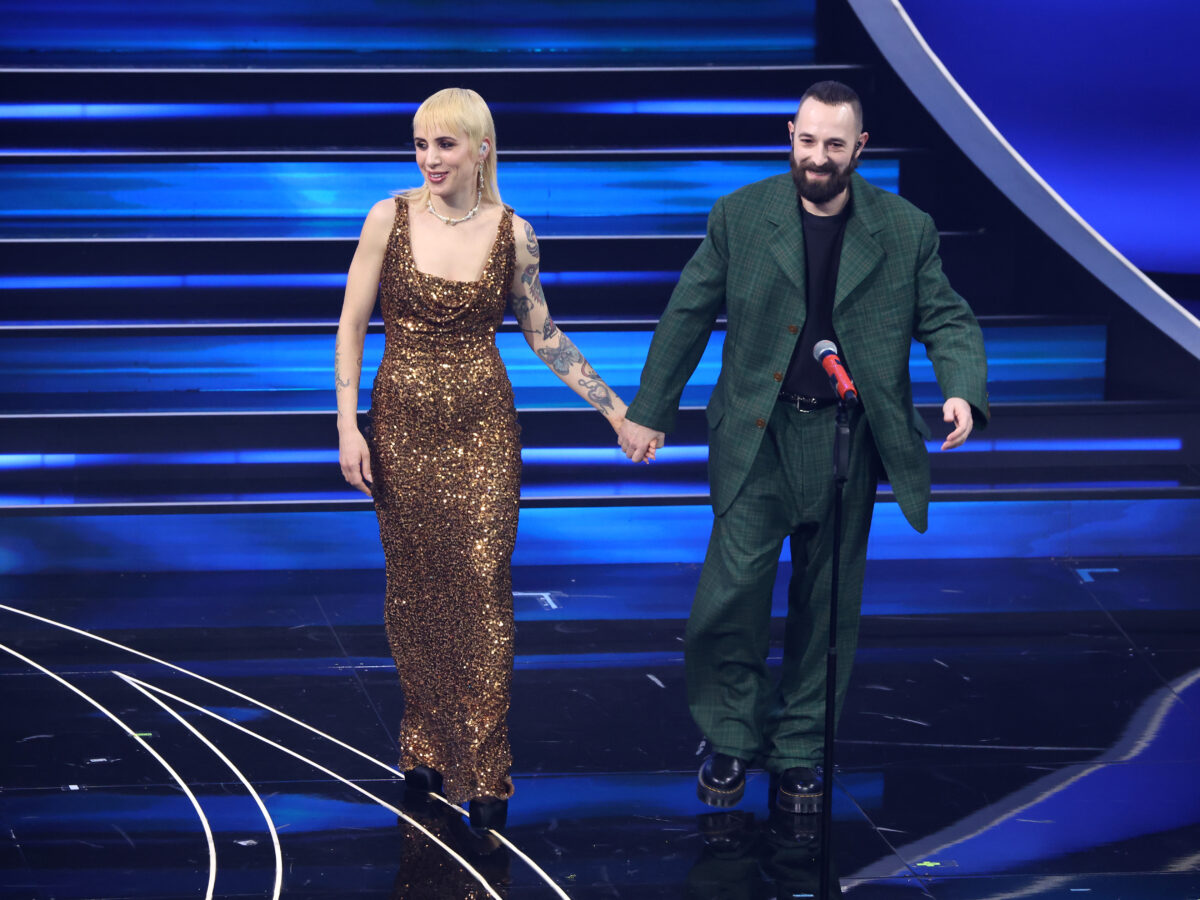 Performativi e romantici come sempre, California e Fausto Lama dei Coma Cose catturano l’attenzione al Festival di Sanremo 2023 celebrando la moda sostenibile di una stilista icona recentemente scomparsa. Parliamo della Madame Vivienne Westwood regina del punk scelta dalla stylist Giorgia Cantarini. Per lei un abito scintillante sui toni del rame e un collier di ossa tempestato di cristalli, per lui un classico completo in tartan britannico verde scuro.