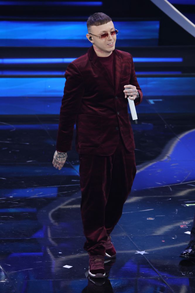 Lazza per la terza serata del Festival di Sanremo 2023. Si presenta con un completo bordeaux in velluto di Missoni progettato da Filippo Grazioli selezionato dallo stylist Simone Furlan. Un completo monocromatico strutturato con blazer indossato sopra ad un top, pantaloni super scivolati e una sneakers più sportiva. E infine un paio di occhiali da sole che riprendono la stessa tonalità del suit.