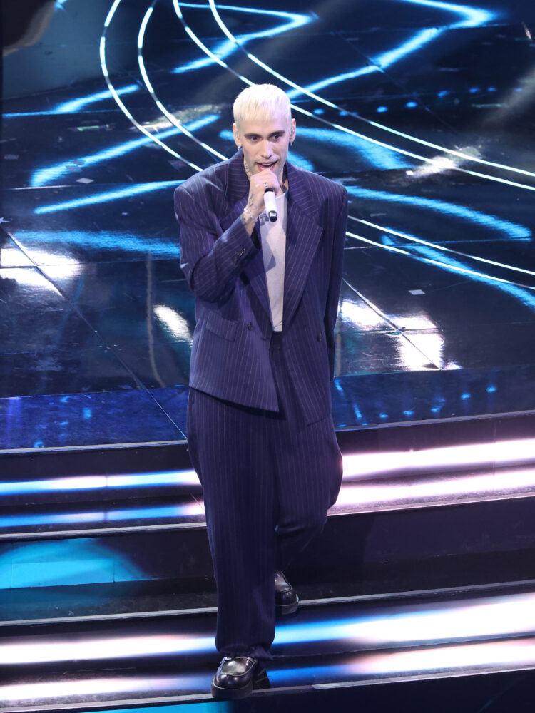 Per la terza serata il cantante Mr.Rain indossa un completo gessato custom in navy blue della collezione autunno inverno 2024 con maglia bianca realizzata in organza di cotone e le scarpe della collaborazione GCDS x Clarks.