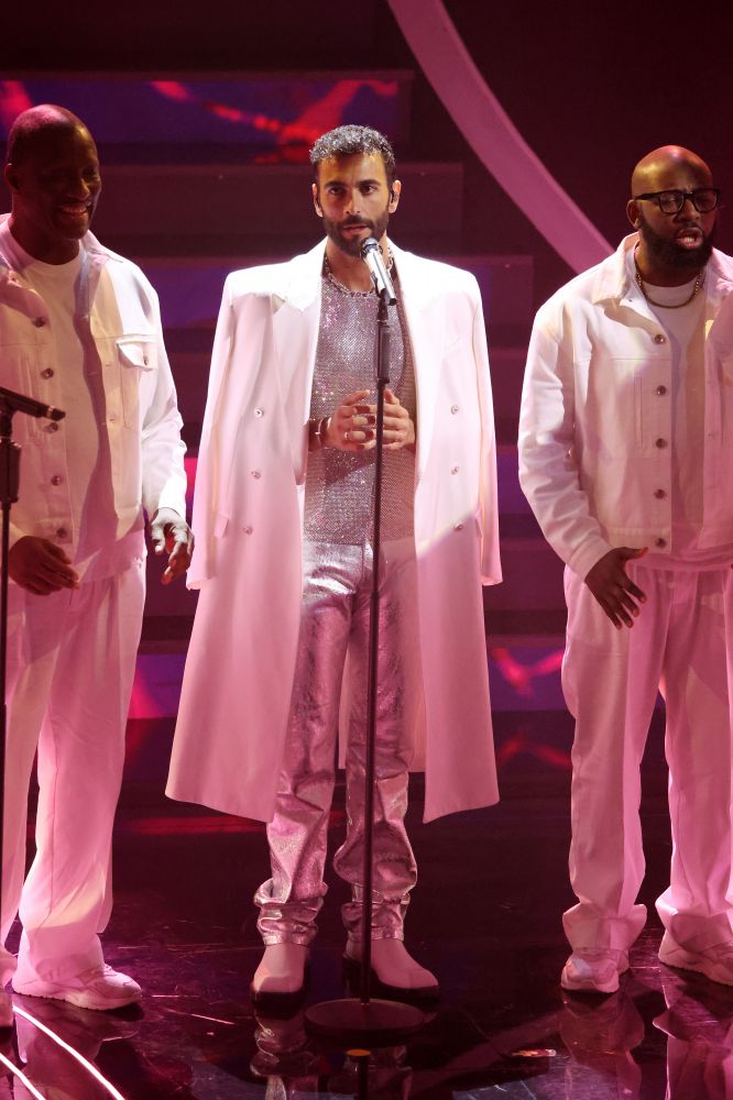 Sempre smanicato, ma questa volta sparkling. Marco Mengoni si per la serata dei duetti si presenta una versione di “Let it be” dei Beatles ma eseguita insieme al coro gospel Kingdom Choir. Si presenta con un cappotto bianco lungo per poi levarselo durante la performance e svelare una canotta smanicata sparkling Versace indossata con un paio di pantaloni lurex argentati e un paio di stivali. Performance brillante, come il suo look.