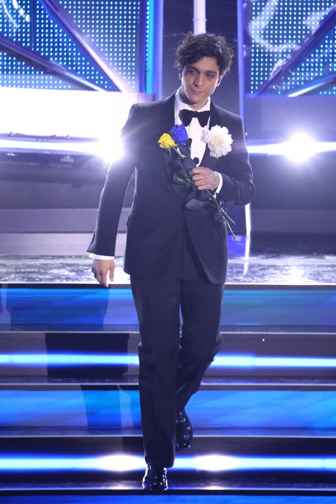 Ancora total look Gucci per Tanani. Questa volta smoking nero con papillon e una spilla a peonia bianca sul revers del blazer. Scende le scale stringendo della mano due rose, una gialla e una azzurra a simboleggiare il supporto per l’Ucraina coinvolta nel conflitto con la Russia