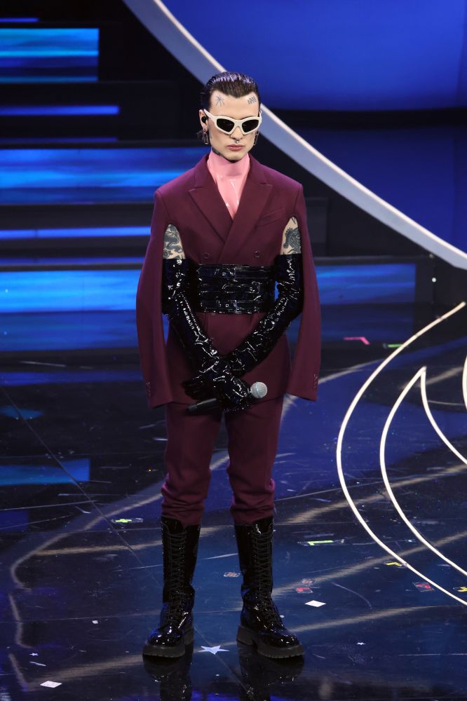 Per la seconda esibizione al Festival di Sanremo, Rosa Chemical indossa un completo in lana bordeaux con giacca stile mantella indossato sopra ad un top in latex rosa. Ad arricchire il look con elementi di styling i guanti lunghi e ampia cintura in vernice nera in perfetto stile bondage.
