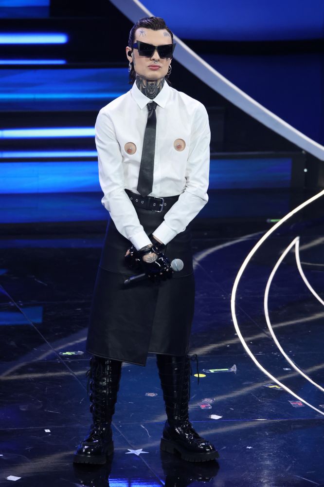 Lo aspettavamo con ansia e per la finale del Festival di Sanremo 2023, Rosa Chemical si presenta con un look Moschino by Jeremy Scott composto con una camicia in cotone bianca con due dettagli laserati sul davanti che svelano i capezzoli abbinati ad una gonna a portafoglio in pelle nera. Completano il look combat boots alti in vernice con lacci e fibbie laterali, cravatta in pelle nera e guanti dallo stile biker. Una performance che si conclude con un limone insieme a Fedez, mentre Chiara Ferragni gli consegna il mazzo di fiori sanremese senza parole.