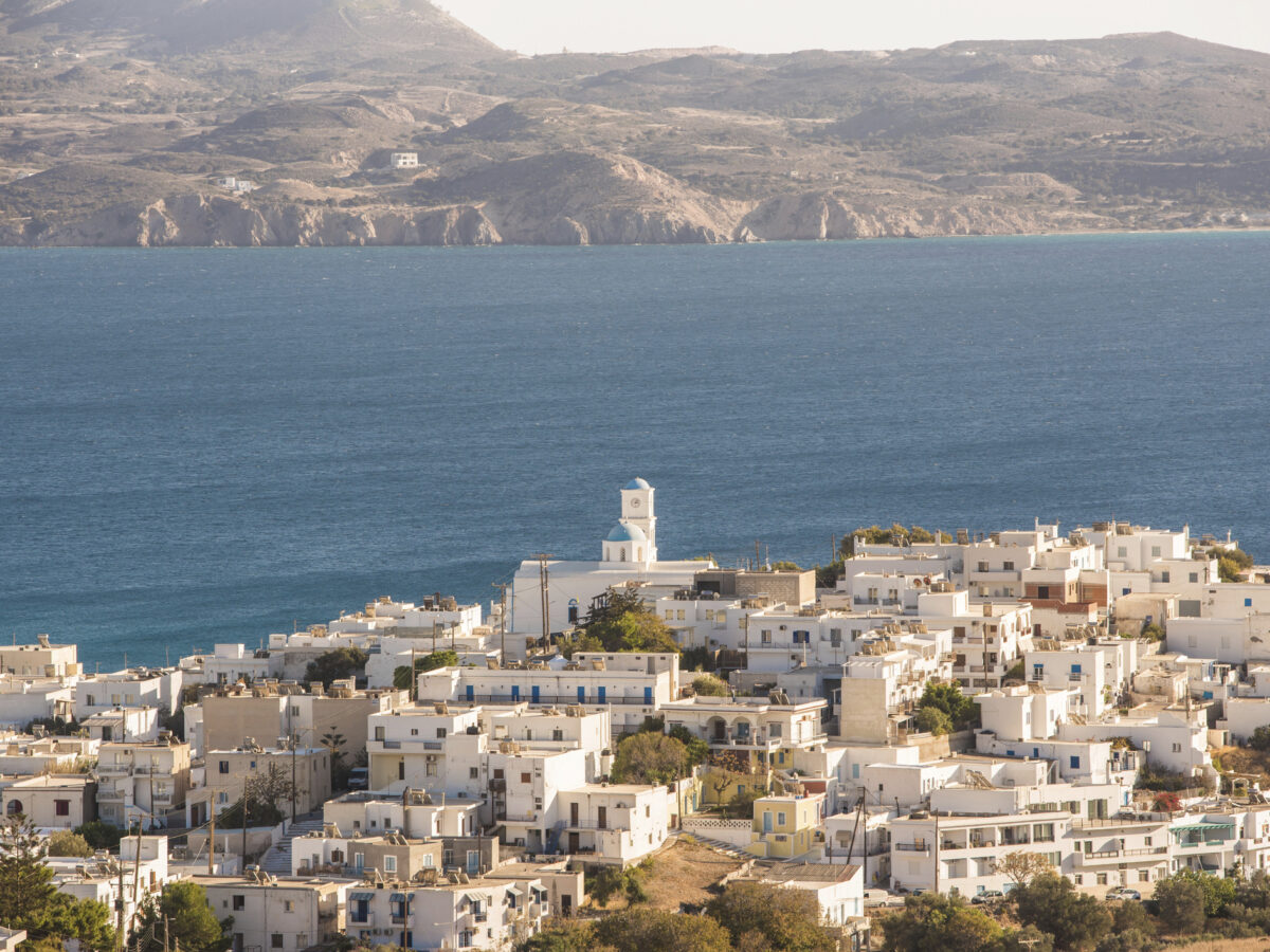 Aerial view of Adamas village on Milos Island, Greece. The scene captures white buildings, a charming church, and the deep blue Aegean Sea, creating a stunning landscape